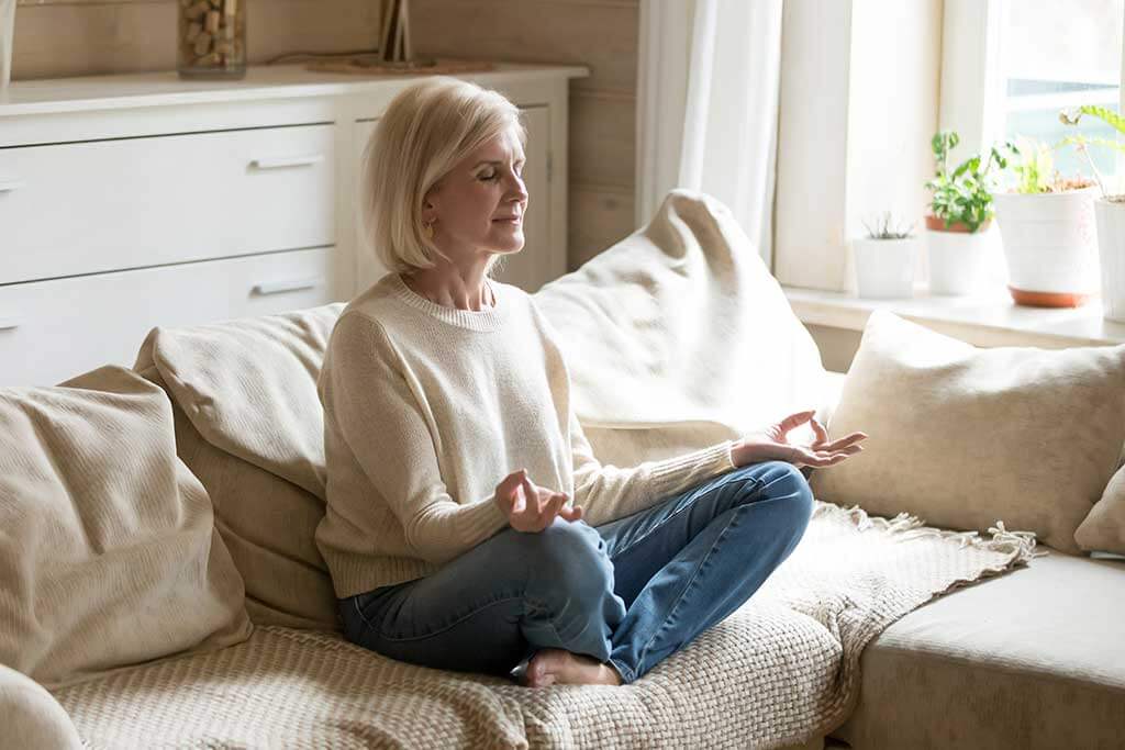 Mindful healthy mature woman practicing meditation at home