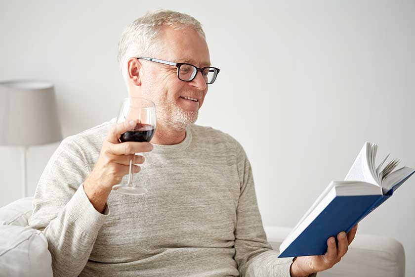 Happy senior man drinking wine and reading book
