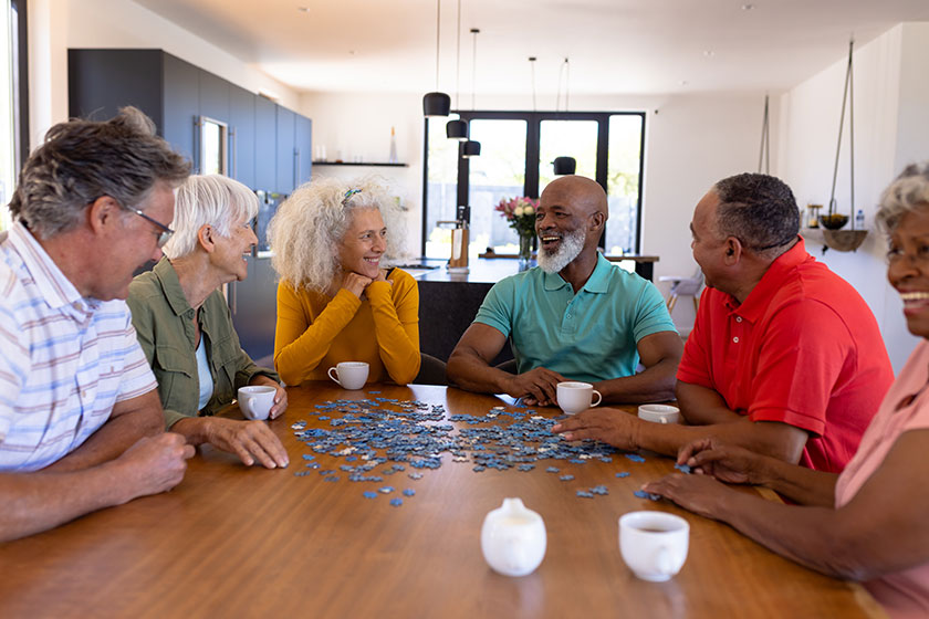 Multiracial seniors friends playing jigsaw puzzle while sitting wooden table