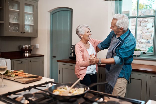 We know how to keep our love going strong. a senior couple dancing while cooking in the kitchen at home