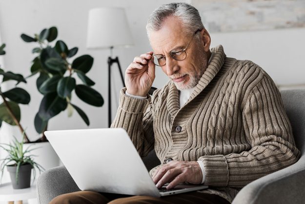 Senior man in glasses looking at laptop at home Senior man in glasses looking at laptop at home
