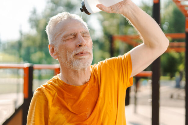Senior man pouring water on head after workout in outdoor gym
