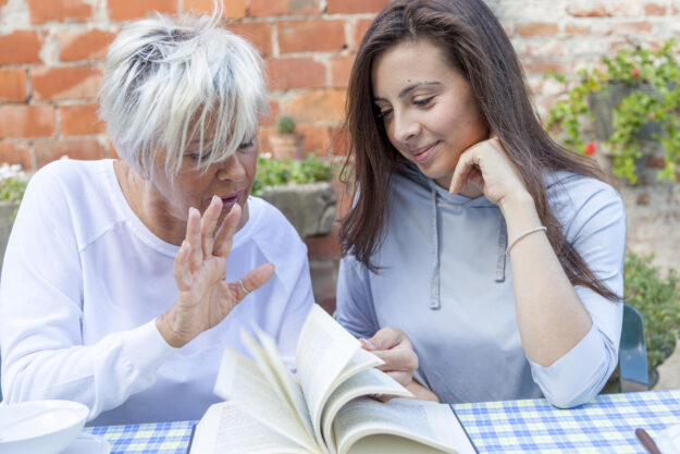pretty mom and daughter reading a book while having breakfast ou